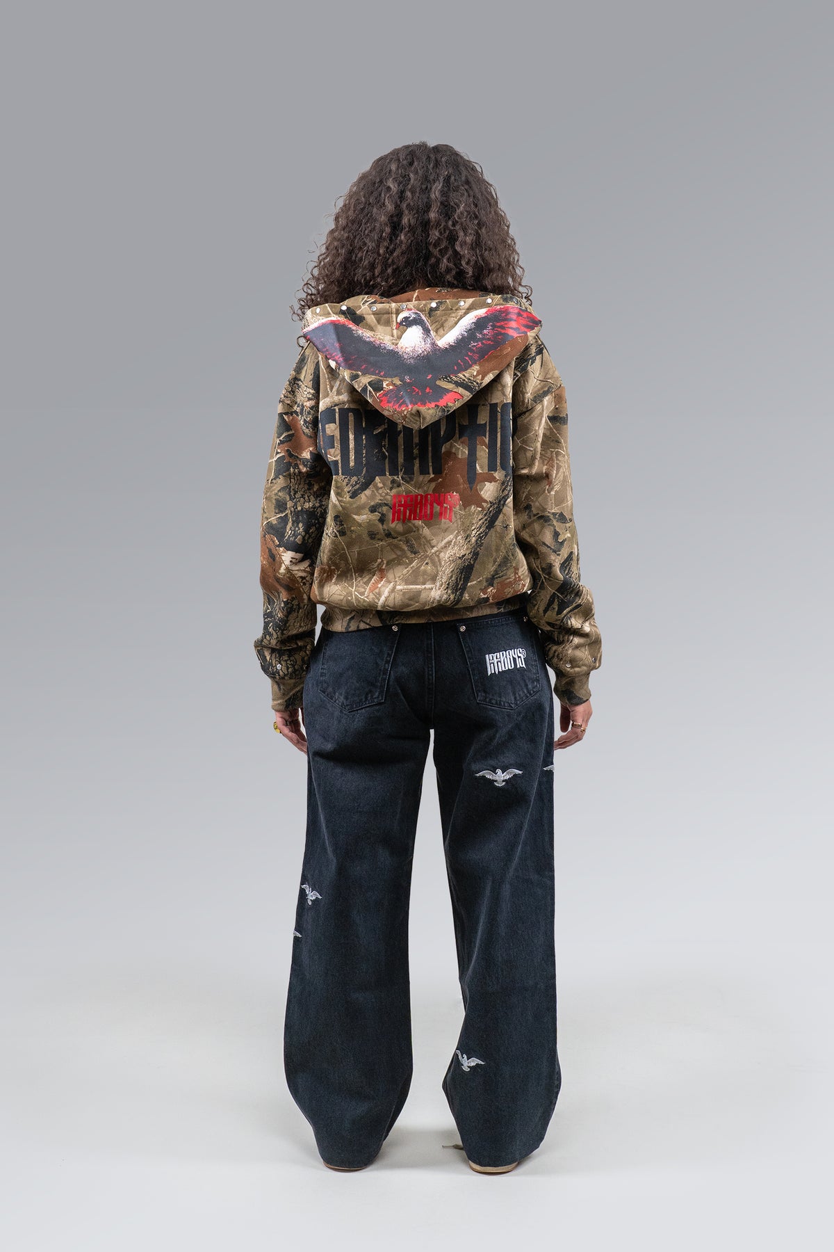 Female model wearing Redemption Camo Zip Hoodie and Redemption Jeans, back view