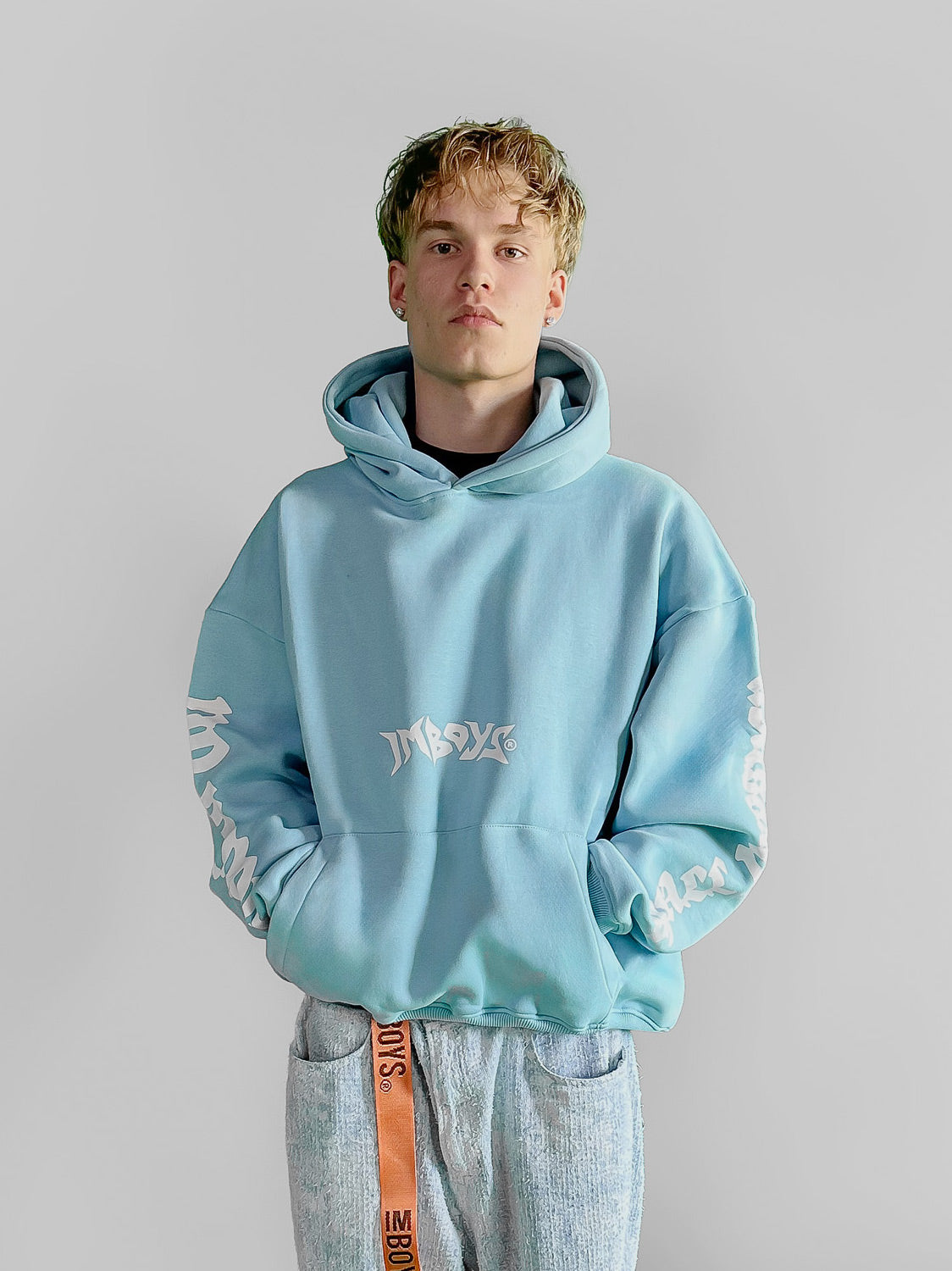 Person wearing a light blue hoodie IMBOYS hoodie on a plain background