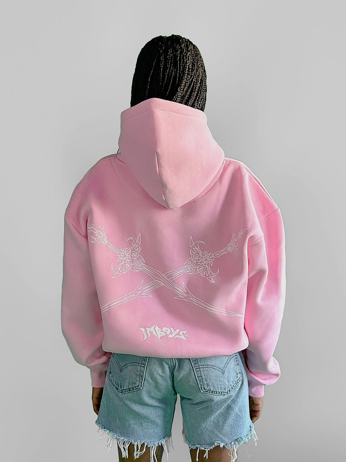 Person wearing a pink hoodie with white designs on the back, standing against a plain background.